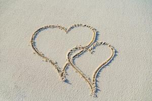 twee harten Aan de strand, tropisch huwelijksreis of verjaardag. tekening in zand met voetstappen. romantisch reizen concept foto