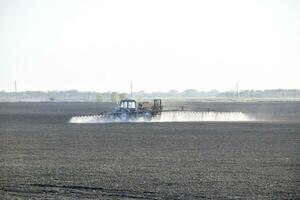 de trekker gespoten herbiciden Aan de veld. chemie in agrarisch foto