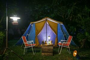 wijnoogst cabine tent, antiek olie lamp, retro stoelen, groep van camping tenten met buitenshuis koffiezetten faciliteiten Aan houten tafels in een Woud camping Oppervlakte in de Woud. foto