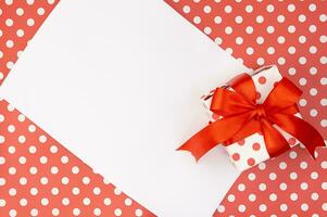 rood polka dots geschenk of Cadeau doos met boog met papier Aan patroon achtergrond. verjaardag, valentijnsdag, moeders en vrouwen dag, vakantie. kopiëren ruimte foto