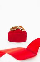 goud bruiloft ringen Aan rood fluweel geschenk doos hart met lint Aan wit achtergrond. huwelijk, voorstel, Valentijnsdag dag. verticaal. kopiëren ruimte foto