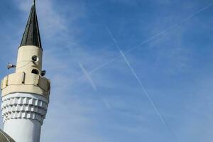 toren van de minaret van de moskee tegen de blauw lucht en de contrail van vliegtuigen. foto