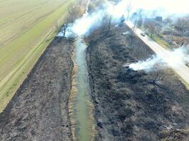 brandend droog gras langs de irrigatie kanaal. rook en de vlam van droog gras. verbrand droog gras. foto