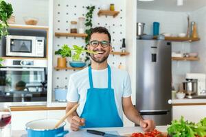 gelukkig knap Mens Koken in keuken Bij huis met selderij in zijn mond poseren voor de foto, gezond leven concept foto