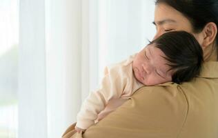 schattig pasgeboren baby meisje slapen Aan moeder schouder in de buurt venster Bij huis foto