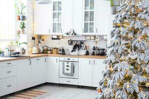 feestelijk Kerstmis decor in wit keuken, modern rustiek interieur met een besneeuwd Kerstmis boom en fee lichten. nieuw jaar, Kerstmis stemming, knus huis. de algemeen plan foto