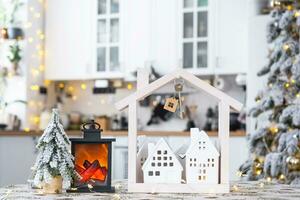 sleutel en klein huis van een klein grootte Aan knus huis met Kerstmis decor Aan tafel van feestelijk wit keuken. geschenk voor nieuw jaar. verzekering, in beweging naar nieuw huis, hypotheek, huur en aankoop echt landgoed foto