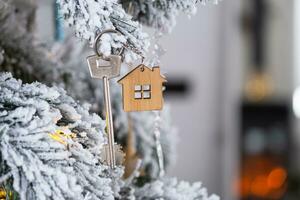 sleutel van het huis met een sleutelhanger hangt aan de kerstboom. een cadeau voor het nieuwe jaar, kerstmis. bouwen, ontwerp, project, verhuizen naar nieuw huis, hypotheek, huur en aankoop onroerend goed. kopieer ruimte foto