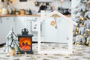 sleutel en klein huis van een klein grootte Aan knus huis met Kerstmis decor Aan tafel van feestelijk wit keuken. geschenk voor nieuw jaar. verzekering, in beweging naar nieuw huis, hypotheek, huur en aankoop echt landgoed foto