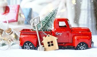 rood retro auto met een Kerstmis boom siert met de huis sleutel in de oppakken vrachtauto voor kerstmis. buying een huis, in beweging, hypotheek, lening, echt landgoed, feestelijk stemming, nieuw jaar foto