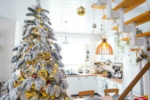 feestelijk Kerstmis decor in wit keuken, modern rustiek interieur met een besneeuwd Kerstmis boom en fee lichten. nieuw jaar, Kerstmis stemming, knus huis. de algemeen plan foto