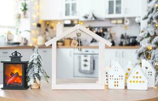 sleutel en klein huis van een klein grootte Aan knus huis met Kerstmis decor Aan tafel van feestelijk wit keuken. geschenk voor nieuw jaar. verzekering, in beweging naar nieuw huis, hypotheek, huur en aankoop echt landgoed foto