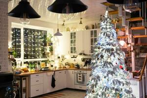 Kerstmis decor in wit keuken, feestelijk troep, dorp interieur met een besneeuwd Kerstmis boom en fee lichten. nieuw jaar, Kerstmis stemming, knus huis. foto