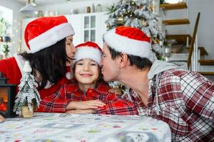 gelukkig traditioneel familie van pa, mama, dochter in feestelijk de kerstman hoeden in een wit keuken met een Kerstmis boom en decor. nieuw jaar, familie waarden. foto