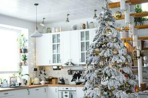 feestelijk Kerstmis decor in wit keuken, modern dorp interieur met een besneeuwd Kerstmis boom en fee lichten. nieuw jaar, Kerstmis stemming, knus huis, metaal modulair trappenhuis. de algemeen plan foto