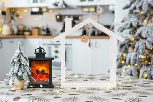 sleutel en klein huis van een klein grootte Aan knus huis met Kerstmis decor Aan tafel van feestelijk wit keuken. geschenk voor nieuw jaar. verzekering, in beweging naar nieuw huis, hypotheek, huur en aankoop echt landgoed foto