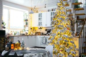 feestelijk Kerstmis decor in wit keuken, modern dorp interieur met een besneeuwd Kerstmis boom en fee lichten. nieuw jaar, Kerstmis stemming, knus huis, metaal modulair trappenhuis. de algemeen plan foto