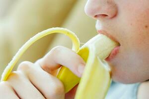 portret van een tiener- jongen aan het eten een banaan. foto van een jongens mond en lippen met een banaan. vers fruit. gezond voedingsmiddelen voor kinderen