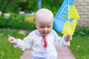 oekraïens vlag in de handen van een gelukkig weinig kind todler in nationaal kostuum. glimlachen kleuter meisje met de vlag van Oekraïne. oekraïens baby maakt de eerste stappen. foto