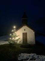 klein kapel met een verlichte Kerstmis boom Bij nacht in de Beiers Alpen foto