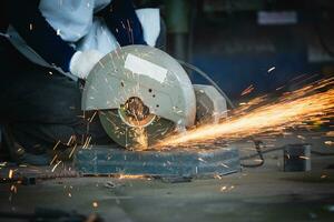 zwaar industrie bouwkunde fabriek interieur met industrieel arbeider gebruik makend van hoek Slijper en snijdend een metaal buis. snijdend metaal en staal met een combinatie circulaire zag met een scherp ronde blad. foto