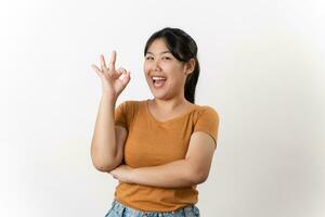 de vrolijk jong Aziatisch vrouw glimlachen en tonen de OK hand- teken staand Aan wit achtergrond. foto