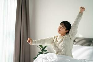 gelukkig vrouw uitrekken haar armen Aan de bed in de ochtend. foto