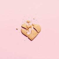 gebroken hart koekjes Aan roze achtergrond. onbeantwoord liefde en gebarsten verhouding concept foto