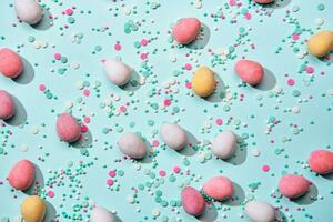 gelukkig Pasen minimaal achtergrond. verstrooiing van chocola eieren in suiker glazuur en suiker sprenkeling Aan blauw achtergrond vlak leggen, moeilijk schaduwen foto