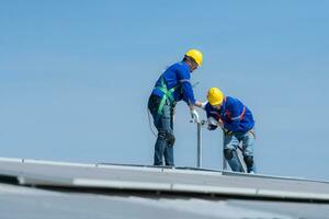 een jong technicus intern werken Aan zonne- panelen is angst van hoogten met senior ingenieurs wie zijn altijd helpen uit foto