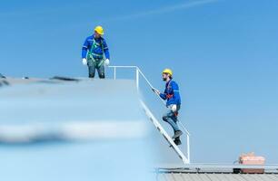 een jong technicus intern werken Aan zonne- panelen is angst van hoogten met senior ingenieurs wie zijn altijd helpen uit foto