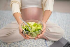 zwanger vrouw aan het eten vers groente salade Bij huis. zwangerschap concept foto