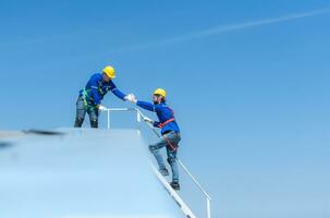 een jong technicus intern werken Aan zonne- panelen is angst van hoogten met senior ingenieurs wie zijn altijd helpen uit foto