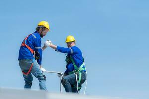 een jong technicus intern werken Aan zonne- panelen is angst van hoogten met senior ingenieurs wie zijn altijd helpen uit foto