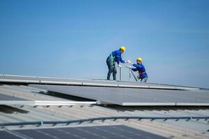 een jong technicus intern werken Aan zonne- panelen is angst van hoogten met senior ingenieurs wie zijn altijd helpen uit foto