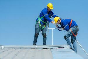 een jong technicus intern werken Aan zonne- panelen is angst van hoogten met senior ingenieurs wie zijn altijd helpen uit foto