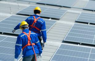 beide van technici is installeren zonne- panelen Aan de dak van de magazijn naar verandering zonne- energie in elektrisch energie voor gebruik in fabrieken. foto