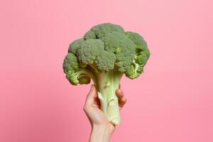 een vrouw hand- houdt een broccoli geïsoleerd Aan een roze achtergrond. foto