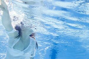 jong meisje in zwempak drijvend Aan azuur water van zwemmen zwembad in zonlicht foto