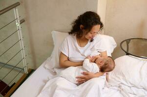 overhead visie van moeder borstvoeding geeft haar pasgeboren baby in de slaapkamer. melk van moeder borst is een natuurlijk geneeskunde voor kinderen. borstvoeding geeft net zo een manier naar verminderen de risico van borst kanker foto