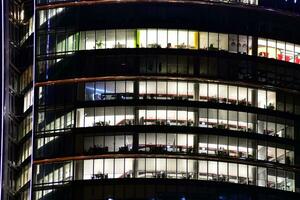 fragment van de glas facade van een modern zakelijke gebouw Bij nacht. modern glas kantoor in stad. groot gloeiend ramen in modern kantoor gebouwen Bij nacht, in rijen van ramen licht schijnt. foto