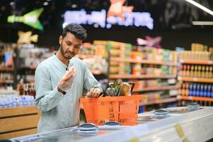 portret van gelukkig Indisch Mens staand in voorkant van de Product teller in een kruidenier op te slaan. Mens buying kruidenier voor huis in supermarkt. foto