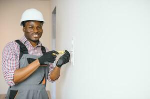 Afro-Amerikaans elektricien gebruik makend van stopcontact Spanning regelgever in kamer foto