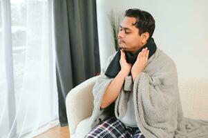 ziek jong Indisch Mens lijden keel pijn terwijl zittend Aan bed Bij huis foto