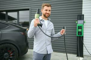 een Mens staat in de buurt een opladen station en kosten zijn elektrisch auto foto