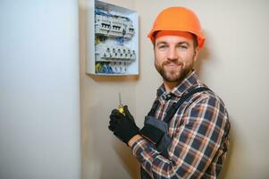 een mannetje elektricien werken in een schakelbord met een elektrisch Verbinden kabel foto