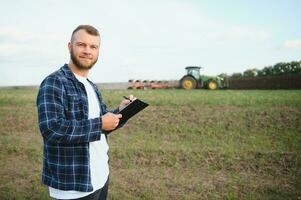 landbouw. boer werken in een veld- in de achtergrond trekker ploegen grond in een veld- van tarwe. landbouw landbouw concept. bedrijf boer in de veld- foto