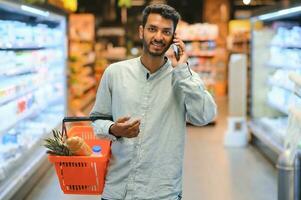 jong Mens gebruik makend van mobiel telefoon terwijl boodschappen doen Bij supermarkt foto