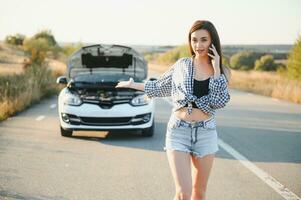 Dames pratend Aan de telefoon over probleem met haar auto ze kan niet. jong sexy meisje overlegt Aan de telefoon gedurende auto reparatie foto