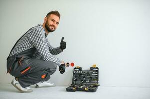 elektricien bouwer Bij werk, installatie van stopcontacten en schakelaars. professioneel in overall met een elektricien hulpmiddel. tegen de achtergrond van de reparatie plaats foto